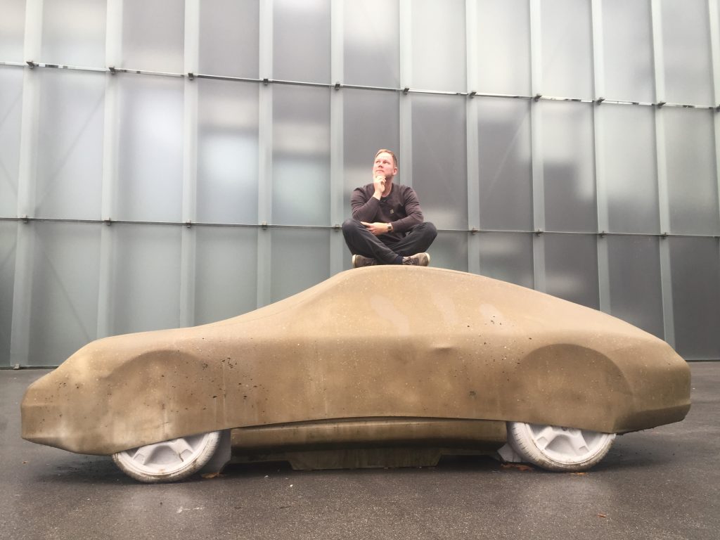 Armin Schobloch sitzt nachdenklich auf einer Betonskulptur in Form eines Autos